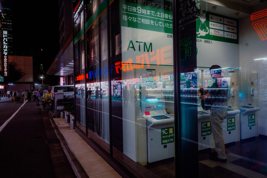 Vetrata di una banca con ATM, passanti e insegne riflesse nella notte, Shinjuku, Tokyo