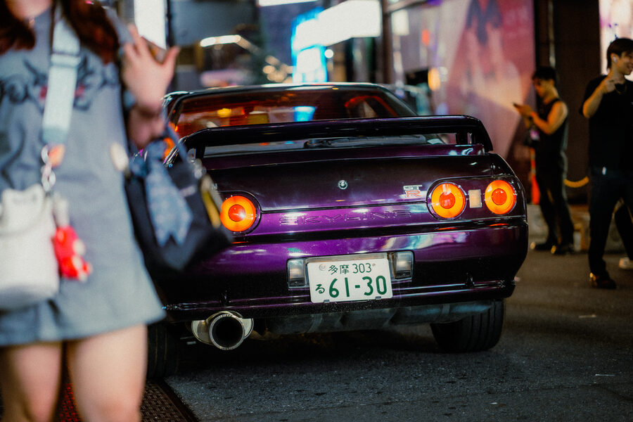 Retro di un’auto sportiva tra i passanti e le luci della notte, Shinjuku, Tokyo
