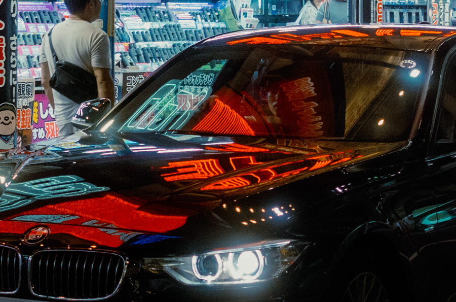 BMW nera ricoperta dai riflessi rossi e azzurri delle insegne, Shinjuku, Tokyo