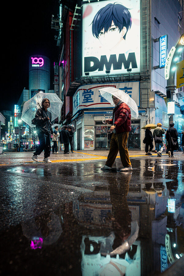 Passanti attraversano Shinjuku tra pioggia e riflessi, Tokyo