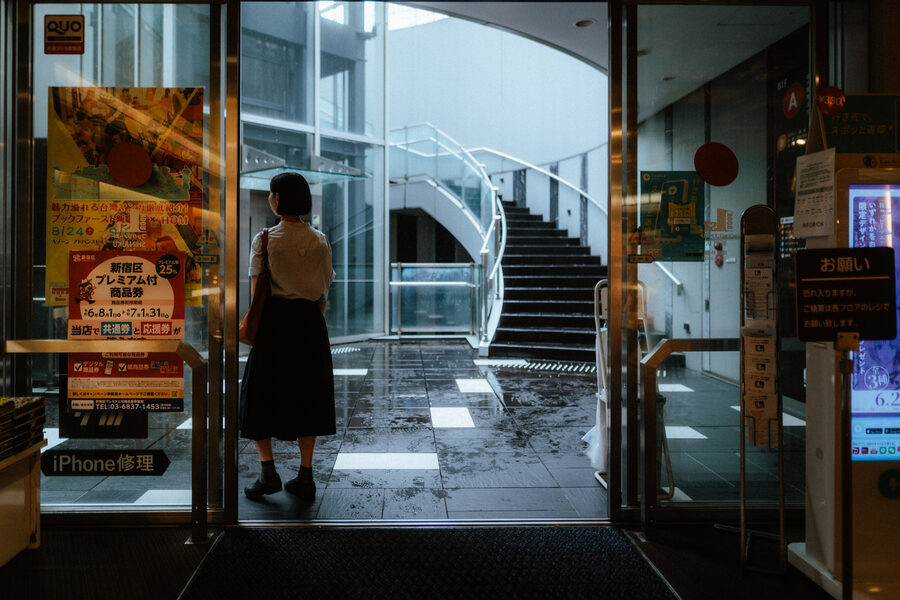 Donna osserva l’esterno dall’ingresso vetrato di un edificio, Shinjuku, Tokyo