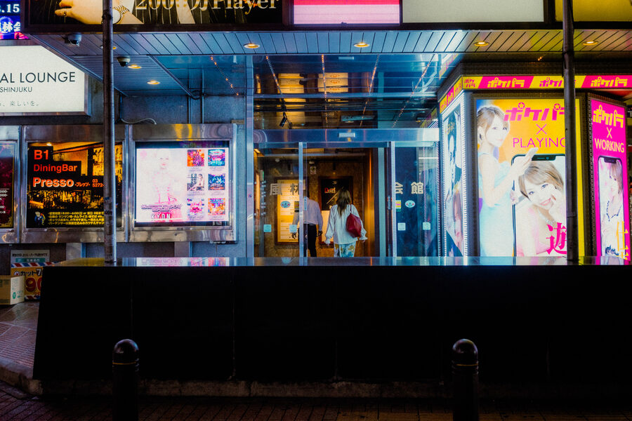 Ingresso di un lounge incorniciato da pannelli pubblicitari rosa e azzurri, Shinjuku, Tokyo