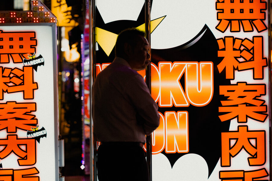 Silhouette di un passante davanti a una grande insegna luminosa, Shinjuku, Tokyo