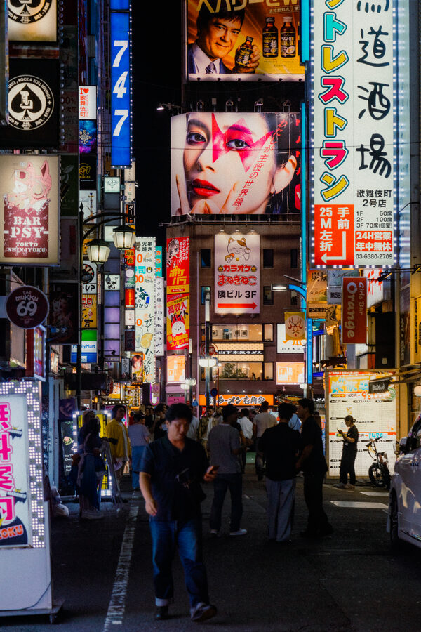 Folla sotto una parete di insegne verticali accese a Kabukichō, Shinjuku, Tokyo