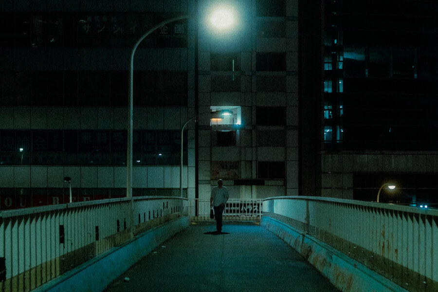 Figura solitaria su una passerella urbana illuminata da un lampione, Shinjuku, Tokyo
