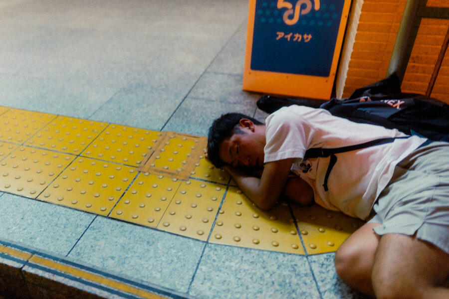 Persona addormentata sul marciapiede accanto a un’insegna, Tokyo