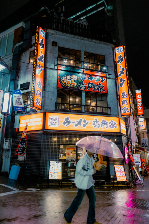 Passante con ombrello tra le insegne di Shinjuku, Tokyo