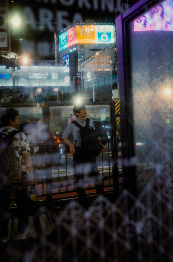 Passanti e insegne sovrapposti nei riflessi di una vetrina notturna, Shinjuku, Tokyo