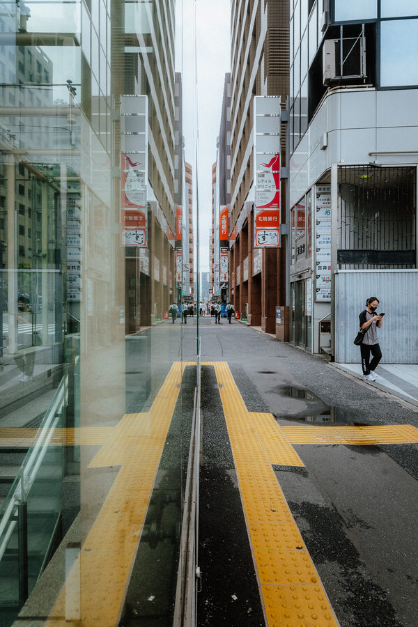 Marciapiede e palazzi si sdoppiano nel riflesso di una grande vetrata, Shinjuku, Tokyo