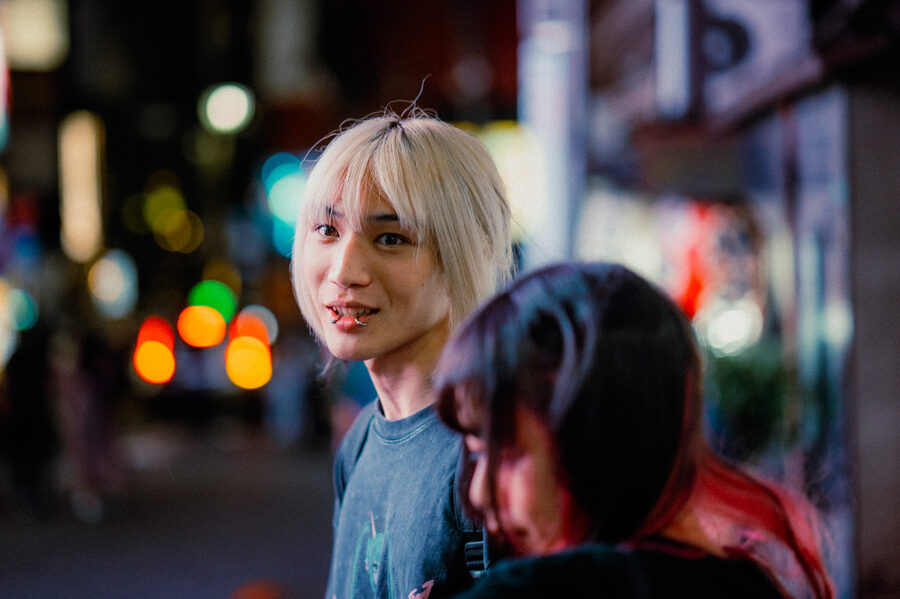 Giovane dai capelli biondi sorride tra le luci sfocate di Shinjuku, Tokyo