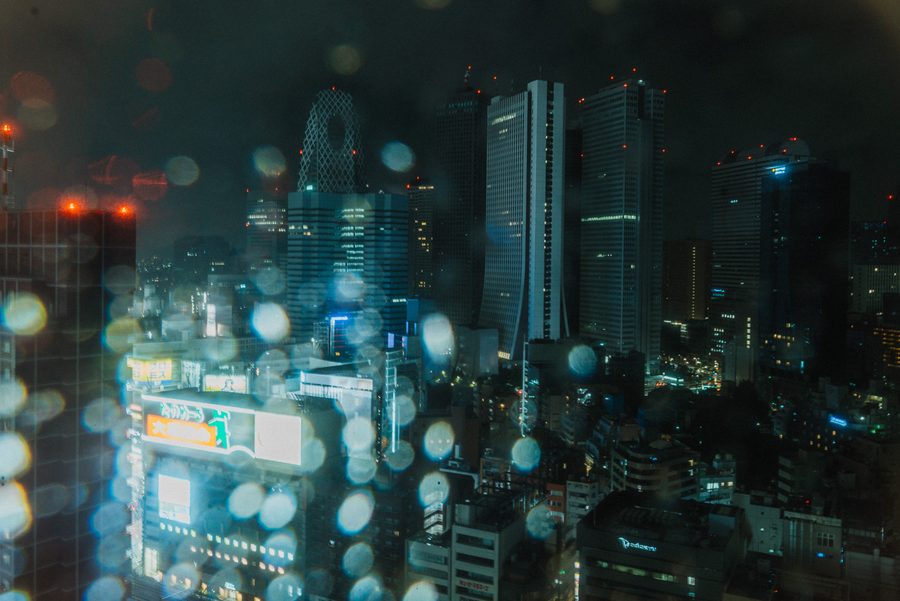 Grattacieli di Nishi-Shinjuku visti dall’alto attraverso una finestra, gocce di pioggia sfocate sul vetro, notte, Tokyo