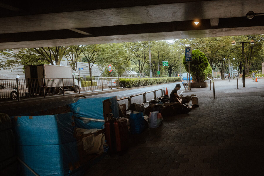 Persone riposano su una panchina sotto una grande struttura urbana, Shinjuku, Tokyo