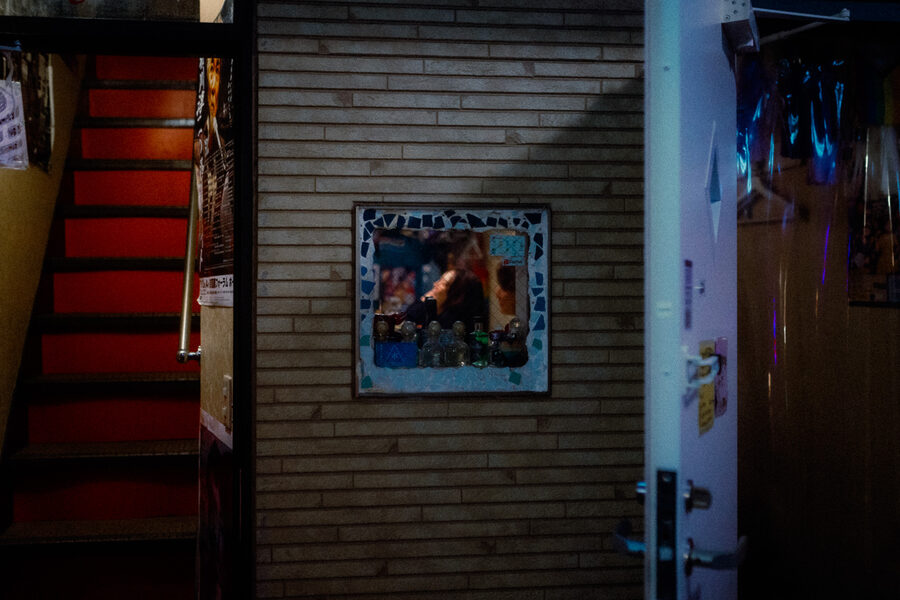 Piccolo specchio su un muro di mattoni tra una scala rossa e una porta azzurra, Shinjuku, Tokyo