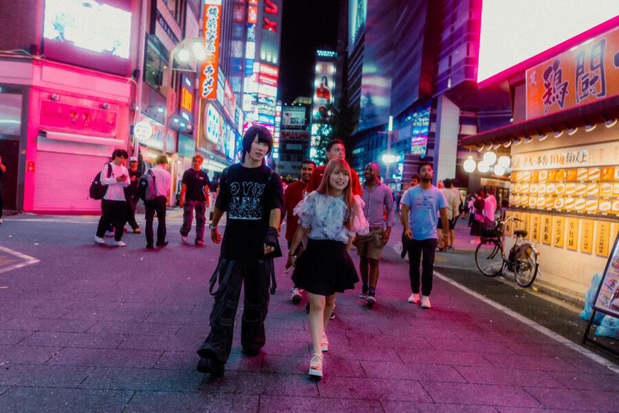 Passanti attraversano una strada immersa nella luce rosa delle insegne, Shinjuku, Tokyo