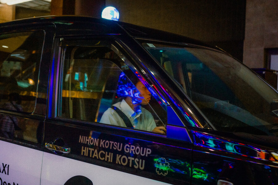 Autista seduto in un taxi nero attraversato dai riflessi blu e viola, Shinjuku, Tokyo