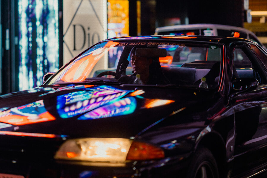 Luci al neon scorrono sul cofano lucido di un taxi nella notte, Shinjuku, Tokyo