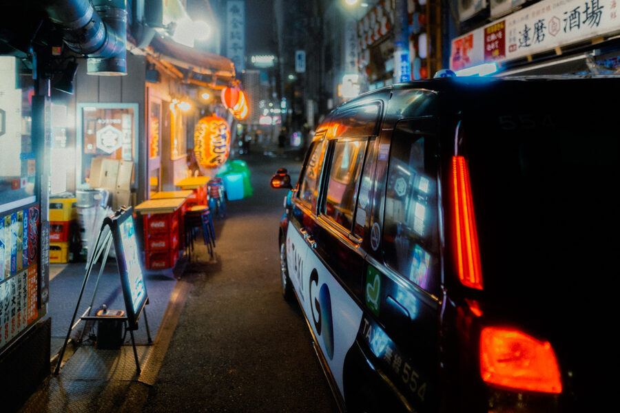 Taxi nero attraversa un vicolo illuminato di Shinjuku, Tokyo