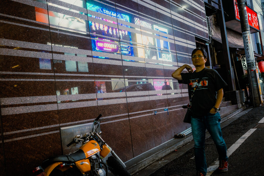 Uomo accanto a una motocicletta davanti alla vetrina illuminata di un negozio, Shinjuku, Tokyo