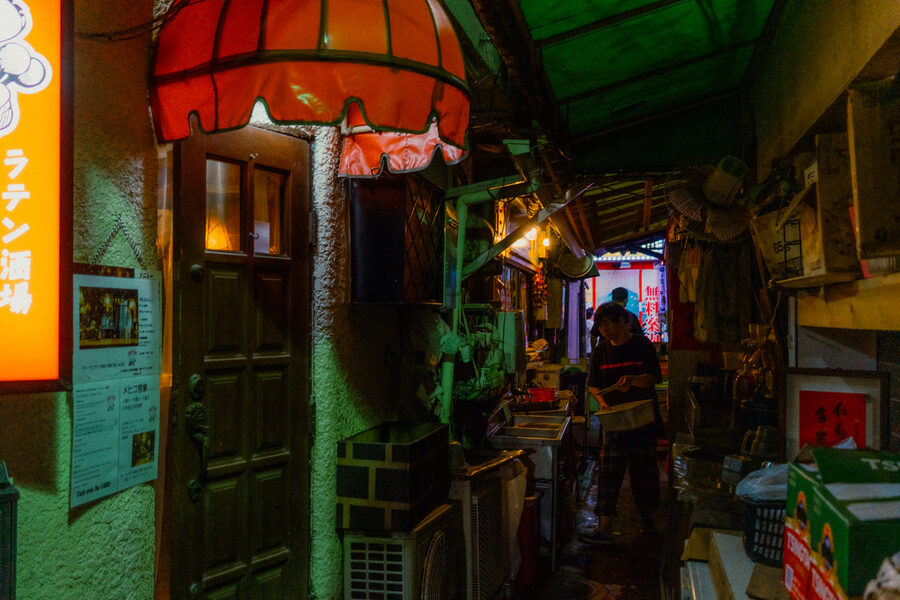 Lavoratrice in un angusto vicolo di servizio sotto una tenda rossa e verde, Shinjuku, Tokyo