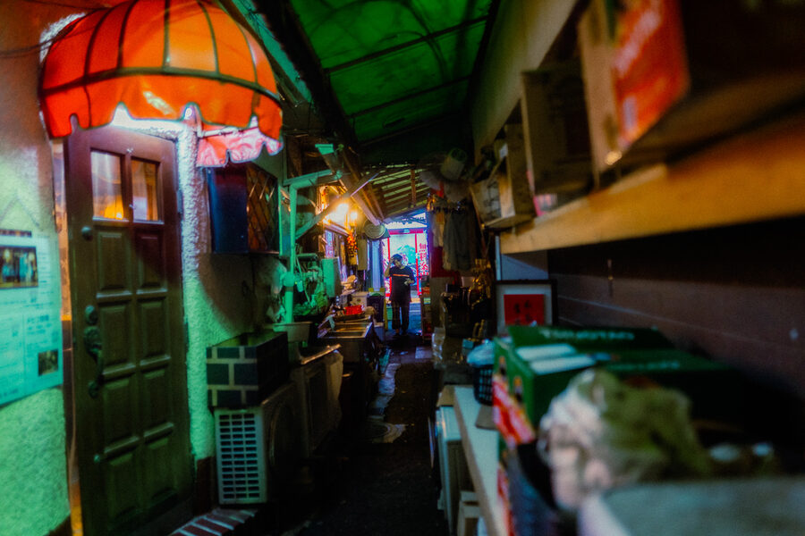 Lungo vicolo di servizio sotto una tenda rossa, con una figura illuminata in fondo, Shinjuku, Tokyo
