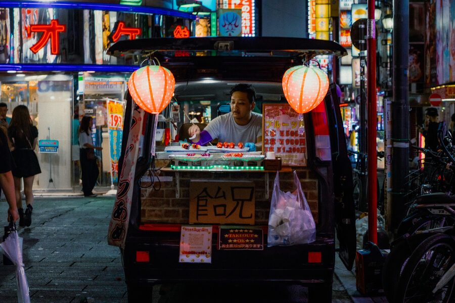 Cuoco dietro il banco di uno yatai incorniciato da due lanterne rosse, Shinjuku, Tokyo