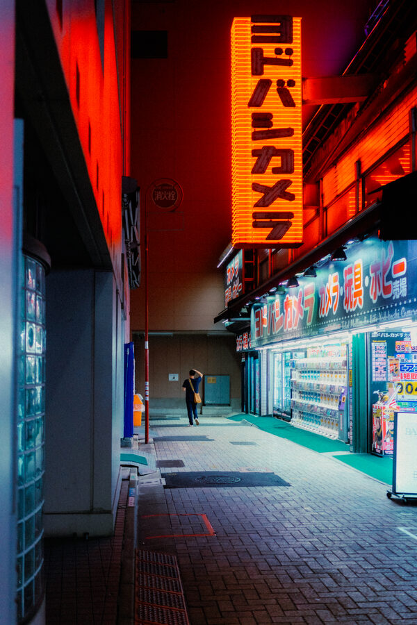 Figura solitaria sotto la grande insegna rossa di Yodobashi Camera, Shinjuku, Tokyo