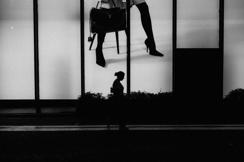 Silhouette in bianco e nero di una donna che cammina davanti a una vetrina di moda, Tokyo