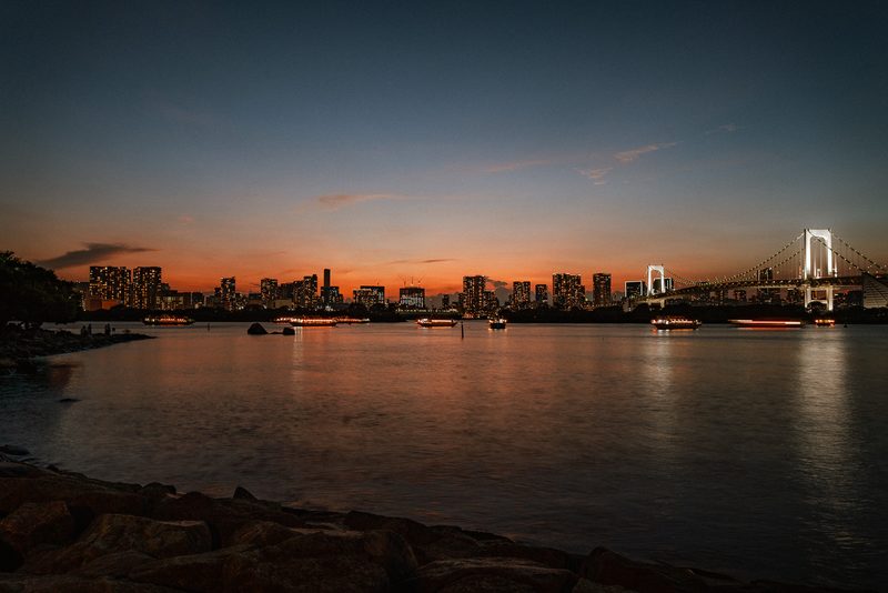 Skyline di Tokyo al tramonto con le barche illuminate e il Rainbow Bridge, baia di Tokyo