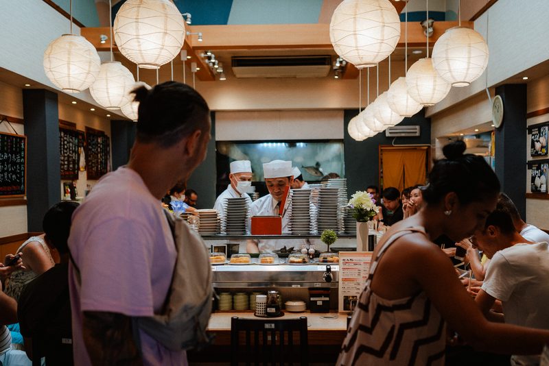 Interno di un sushi con lanterne di carta bianche, chef e avventori, mercato di Tsukiji, Tokyo