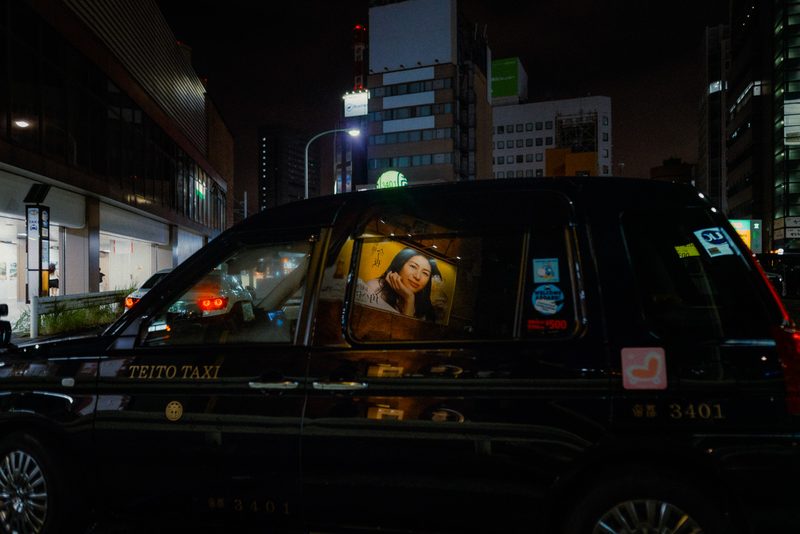 Taxi Teito di notte con un manifesto illuminato nel finestrino, Tokyo