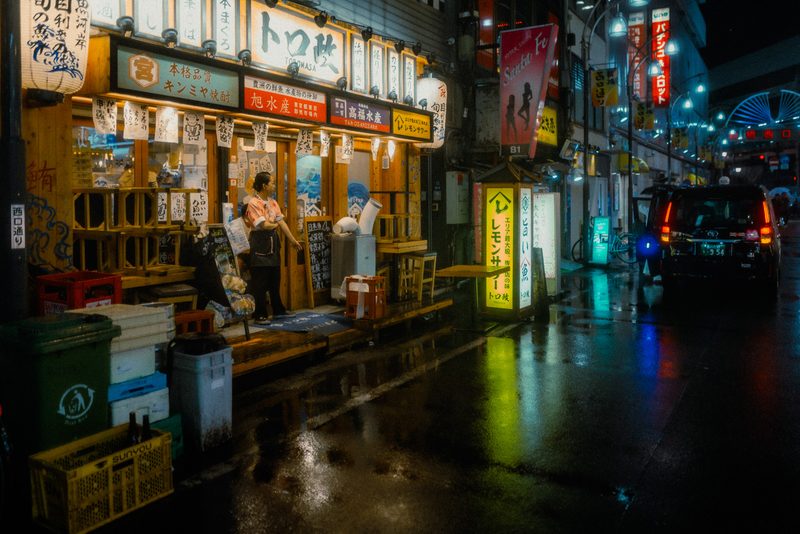 Facciata dell'izakaya Toromasa con lanterne e insegne al neon, addetta sulla soglia, notte di pioggia, Tokyo