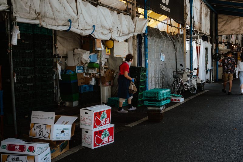 Addetta del mercato tra scatole di cocomeri e casse, retro di Tsukiji, di giorno, Tokyo