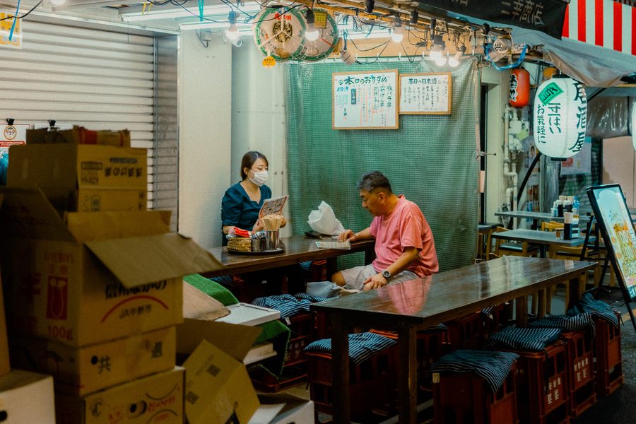 Cliente legge il menù ai tavoli all’aperto di un izakaya, cameriera dietro il bancone, Ueno, Tokyo