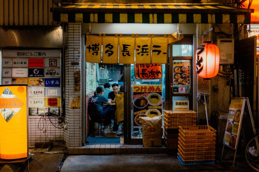 Clienti al banco di un piccolo ramen-ya dietro il noren giallo, lanterna rossa accesa, Ueno, Tokyo