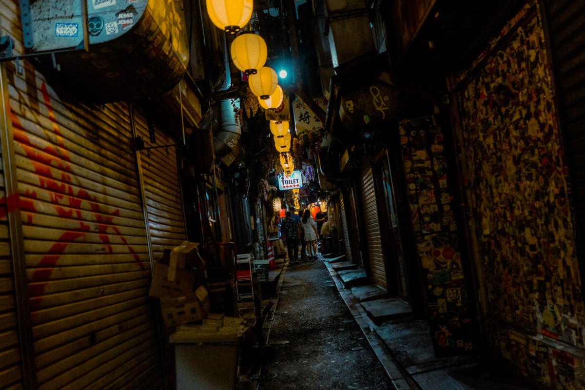Lanterne accese sopra un vicolo di serrande chiuse coperte di adesivi, Shinjuku, Tokyo