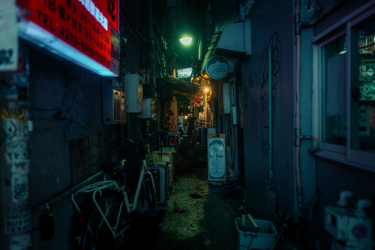 Vicolo di servizio illuminato da un lampione verde, con biciclette e cassette, Shinjuku, Tokyo