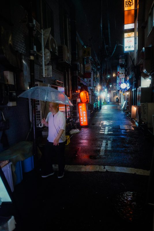 Uomo con ombrello trasparente in un vicolo stretto accanto a un'insegna rossa di yakitori, notte di pioggia, Tokyo