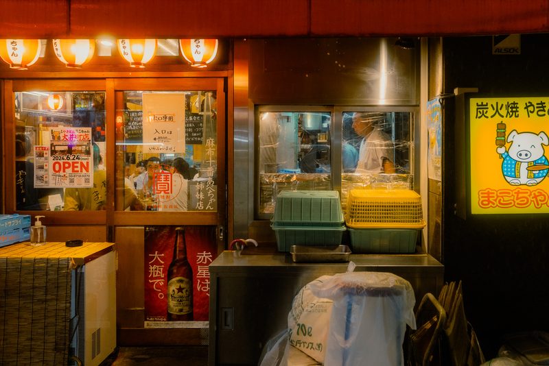 Cuoco al lavoro dietro il vetro di uno yakitori con lanterne rosse, di notte, Tokyo
